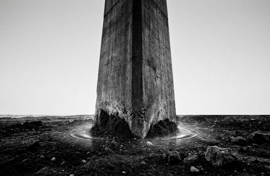 A high-contrast black and white photograph of a solid stone pillar anchored deeply into the ground, symbolizing the permanence and resilience of an omnipresent marketing infrastructure.